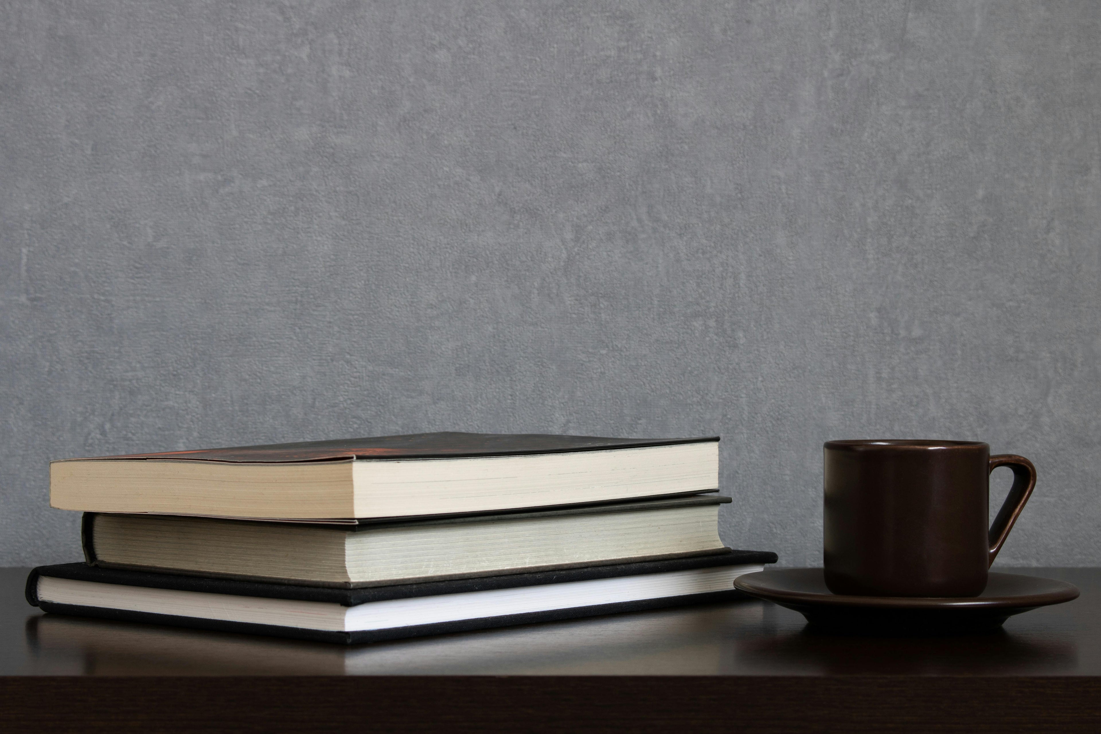 A stack of books next to a coffee cup on a wooden table